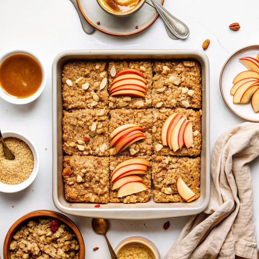 A square of warm apple cinnamon baked oatmeal in a bowl, topped with yogurt and apple slices.
