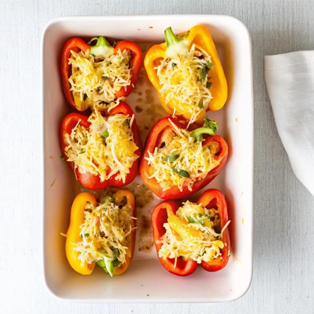 A baking dish filled with cheesy chicken and rice stuffed bell peppers, topped with crackers and parsley.