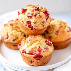Freshly baked cranberry orange muffins with a sweet glaze and orange zest garnish on a wooden board.