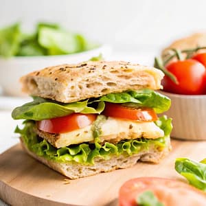 A toasted pesto chicken sandwich filled with shredded chicken coated in basil pesto, fresh tomatoes, mozzarella, and spinach on golden crispy bread.