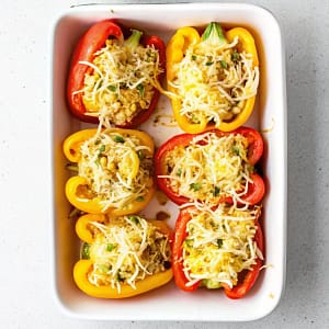 A baking dish filled with cheesy chicken and rice stuffed bell peppers, topped with crackers and parsley.