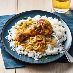 A skillet of creamy Smothered Chicken and Rice, showing golden chicken thighs nestled in fluffy rice and a rich mushroom gravy, garnished with parsley.