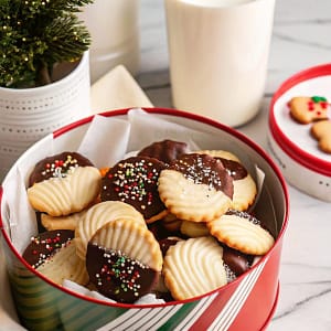 A festive assortment of chocolate dipped butter cookies with holiday sprinkles on a wooden board.